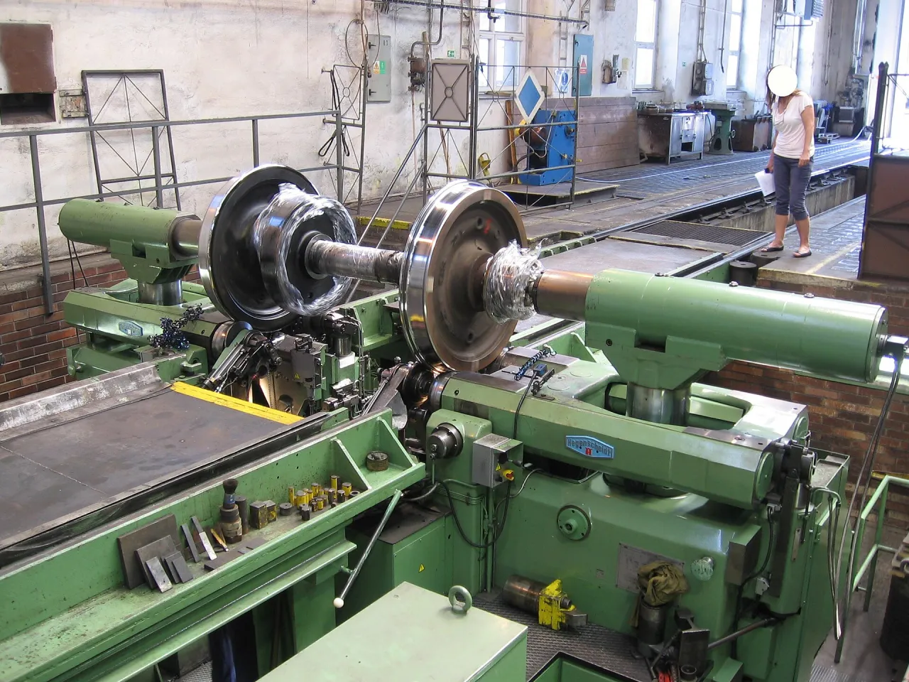 A railway wheelset being machined on a Hegenscheidt wheel lathe, with an engineer alongside